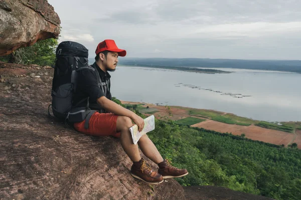 Человек путешественник с рюкзаком сидит на краю скалы, на вершине — стоковое фото