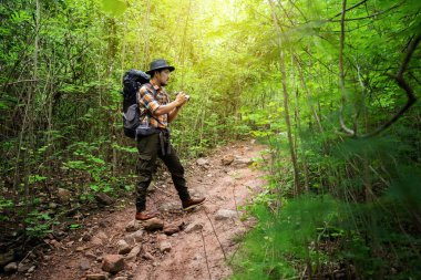 Gezgin adam ormanda sırt çantalı bir kamera tutuyor.