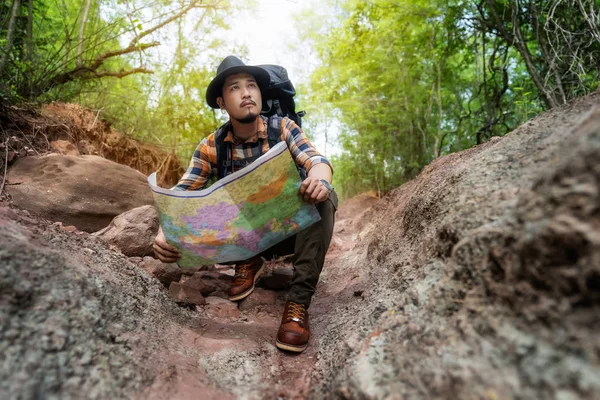 Homme voyageur avec sac à dos assis et la carte de lecture dans la forêt — Photo
