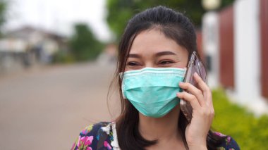 Tıbbi maskeli genç bir kadın cep telefonuyla konuşuyor, koronavirüs koruması.