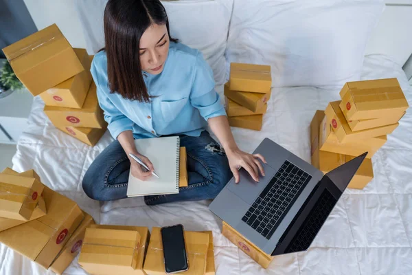 自宅のベッドでノートパソコンを使ってオンラインで製品を販売している若い女性は — ストック写真