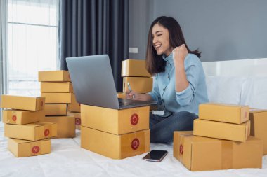 Başarılı bir kadın evdeki bir yatakta online ürün satmak için dizüstü bilgisayar kullanıyor.
