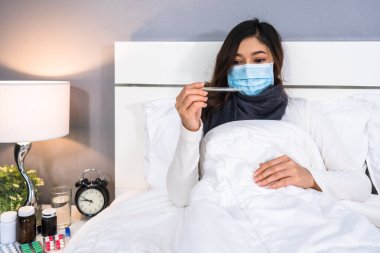 Sıcaklığını ölçmek için termometre kullanan maskeli hasta kadın, koronavirüs (covid-19) pandemik konsept.