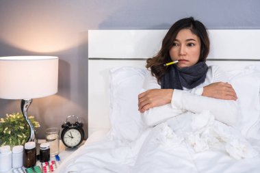 Hasta kadın üşüyor ve termometreyi yatakta ateşini ölçmek için kullanıyor.