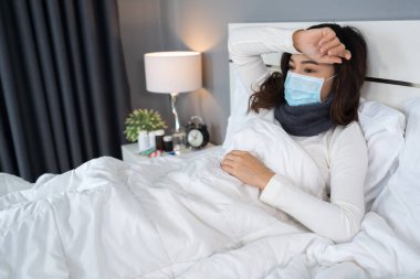 Tıbbi maskeli hasta kadın baş ağrısı ve virüsten muzdarip ve yatakta ateş, koronavirüs (covid-19) pandemik konsept.