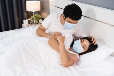 Adam hasta karısına evde bir yatakta bakıyor, Coronavirus 'u korumak için tıbbi maske takan çift (covid-19)
