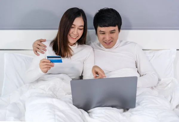 couple using laptop computer to shopping online with credit card on a bed