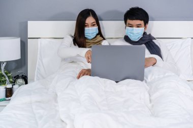Karantina sırasında dizüstü bilgisayar kullanan tıbbi maskeli çift koronavirüs (covid-19) evde kalır..