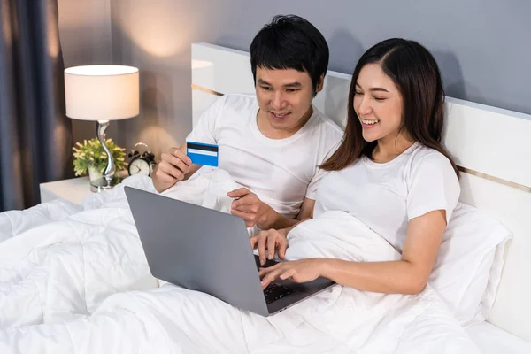 couple using laptop computer to shopping online with credit card on a bed