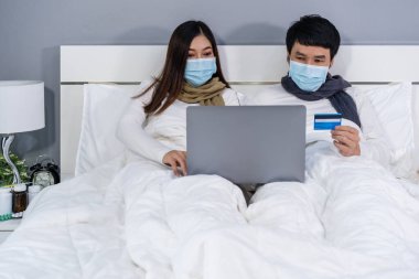 Karantina pandemik koronavirüsü (covid-19) sırasında kredi kartıyla online alışveriş yapmak için dizüstü bilgisayar kullanan çift evde kalıyor..