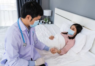 Hasta kadın yatakta yatarken doktor nabzını kontrol ediyor olmalı. İnsanlar koronavirüsten (covid-19) korunan tıbbi maske takıyor olmalı.