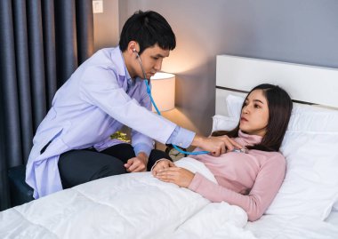 Doktor, hasta bir kadının kalbini dinlemek için steteskop kullanıyor.