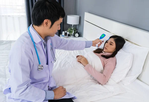 doctor using infrared forehead thermometer (thermometer gun) to measuring temperature of sick woman on a bed