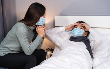 Eş hasta kocasına evde bir yatakta bakıyor, insanlar koronavirüsten korunmak için tıbbi maske takıyor olmalı (covid-19).