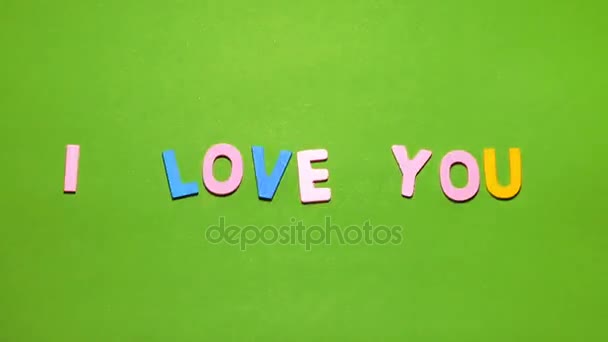 Holzfiguren in verschiedenen Farben in einem Wort Valentinstag auf grünem Hintergrund mit Unschärfeeffekt angeordnet — Stockvideo