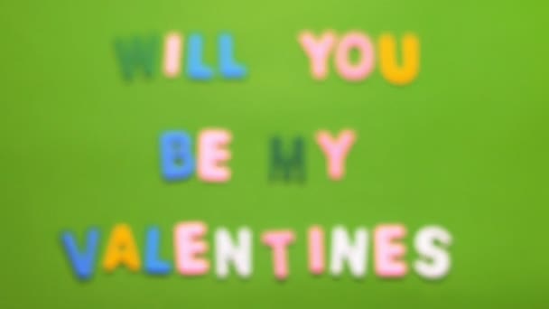 Holzfiguren in verschiedenen Farben in einem Wort Valentinstag auf grünem Hintergrund mit Unschärfeeffekt angeordnet — Stockvideo