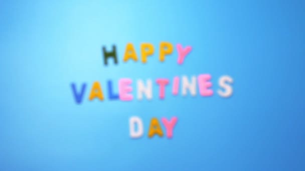 Personajes de madera de diferentes colores dispuestos en una palabra Día de San Valentín sobre un fondo verde con efecto borroso — Vídeos de Stock