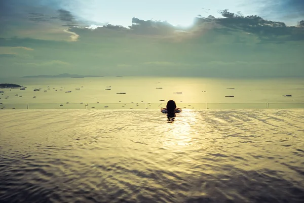 A sziluett, egy nő a medence fedélzet, a tető, a társasház, a tengerre és a naplementére. — Stock Fotó