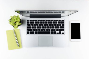 Beyaz ofis masası, beyaz akıllı telefon, boş ekran, defter, dizüstü bilgisayar ve malzemeler..