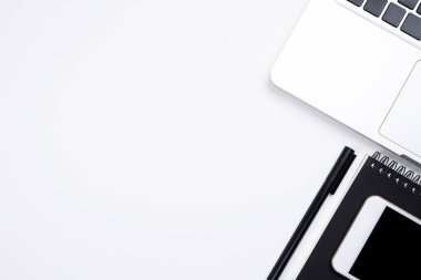 Beyaz ofis masası, beyaz akıllı telefon, boş ekran, defter, dizüstü bilgisayar ve malzemeler..