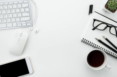 Beyaz ofis masası, beyaz akıllı telefon, boş ekran, defter, dizüstü bilgisayar ve malzemeler..