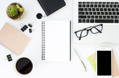 Beyaz ofis masası, beyaz akıllı telefon, boş ekran, defter, dizüstü bilgisayar ve malzemeler..