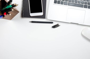 Laptop ve malzemelerle dolu beyaz masa. Kopyalama alanı olan üst görünüm, düz yatay.