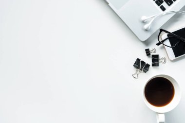 Laptop, kahve ve malzemelerle dolu beyaz ofis masası. Kopyalama alanı olan üst görünüm, düz yatay.