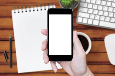 Ahşap ofis masasının üzerinde boş ekranlı akıllı telefonu tutan..