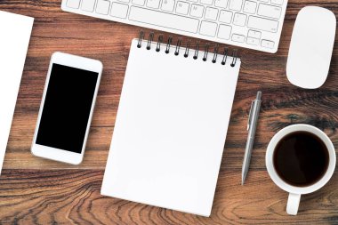 Boş defterli ahşap masa, bilgisayar gereçleri ve ofis malzemeleri. Üst manzara, düz uzanma.