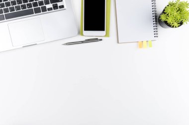 Beyaz ofis masası, beyaz akıllı telefon, boş ekran, defter, dizüstü bilgisayar ve malzemeler..