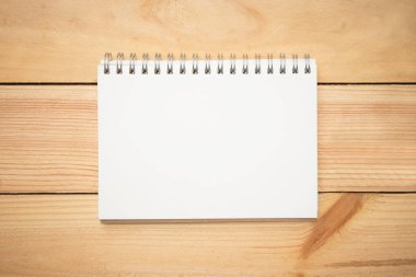 Ahşap ofis masasının ortasında boş bir defter sayfası. Üst manzara, düz uzanma.