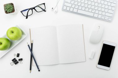 Beyaz ofis masası, beyaz akıllı telefon, boş ekran, defter, dizüstü bilgisayar ve malzemeler..