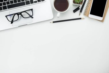 Beyaz ofis masası, beyaz akıllı telefon, boş ekran, defter, dizüstü bilgisayar ve malzemeler..