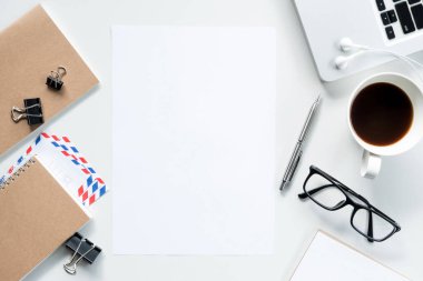 Boş bir a4 kağıdı beyaz ofis masasının ortasında. Üst manzara, düz uzanma.