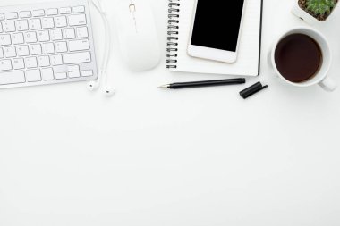 Beyaz ofis masası, beyaz akıllı telefon, boş ekran, defter, dizüstü bilgisayar ve malzemeler..