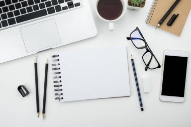 Beyaz ofis masası, beyaz akıllı telefon, boş ekran, defter, dizüstü bilgisayar ve malzemeler..