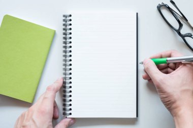 Erkek eli boş defter sayfasına bir şeyler yazacak ahşap ofis masasının üstüne..