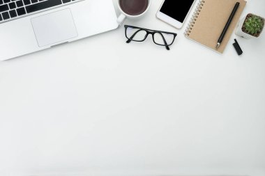 Beyaz ofis masası, beyaz akıllı telefon, boş ekran, defter, dizüstü bilgisayar ve malzemeler..