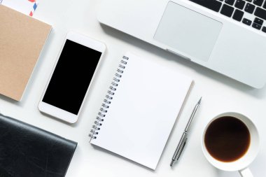 Boş defter sayfası ve malzemeleri olan beyaz ofis masası. Kopyalama alanı olan üst görünüm, düz yatay.