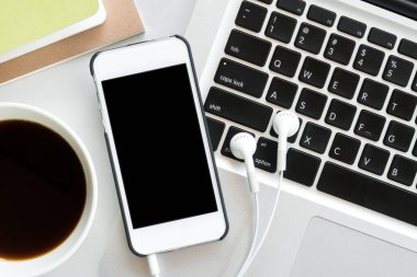 Beyaz ofis masası, beyaz akıllı telefon, boş ekran, defter, dizüstü bilgisayar ve malzemeler..