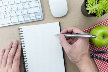 Erkek eli boş defter sayfasına bir şeyler yazacak ahşap ofis masasının üstüne..