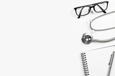 Steteskop defteri ve kalem ve gözlüklü beyaz doktor masası. Kopyalama alanı olan üst görünüm, düz yatay.