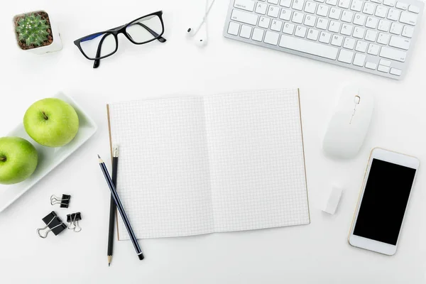 White office desk table with white smartphone with blank screen, notebook, laptop computer and supplies.