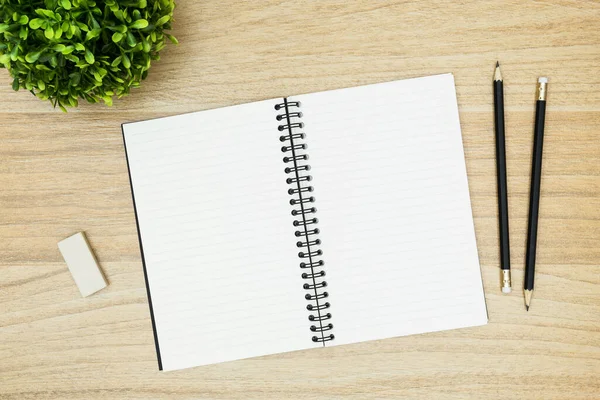 Silgi ve kalemlerle dolu boş bir defter ahşap masanın üzerinde. Üst manzara, düz uzanma.