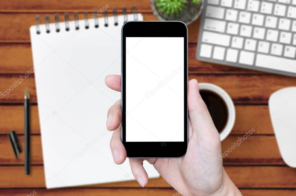Hand holding smartphone with blank screen over the wood office table.