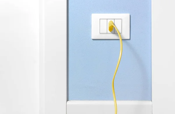 Plug amarelo em um soquete de parede em uma parede azul — Fotografia de Stock