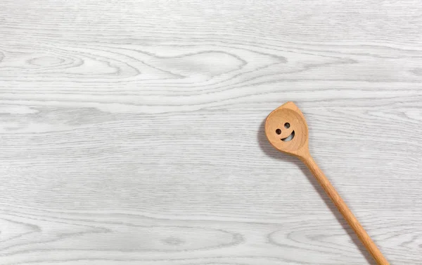 Cucchiaio di legno sorridente su uno sfondo di legno bianco — Foto Stock