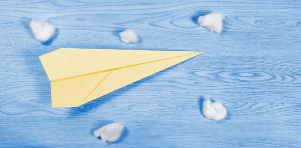 Żółty Papierowy Samolot Wśród Bawełnianych Kulek Nad Drewnianym Niebieskim Tłem — Zdjęcie stockowe