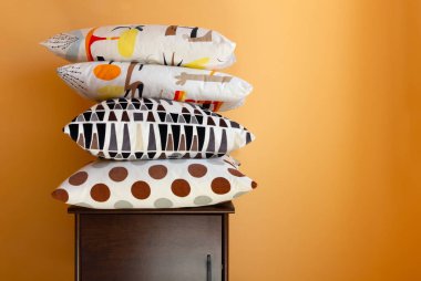 Ahşap bir komodinin üzerindeki yastık yığını turuncu renkli bir iç duvara karşı.